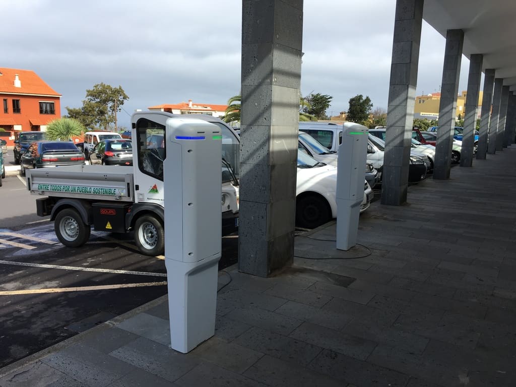varios vehículos eléctricos en estación de recarga. En primer término un tótem de recarga blanco
