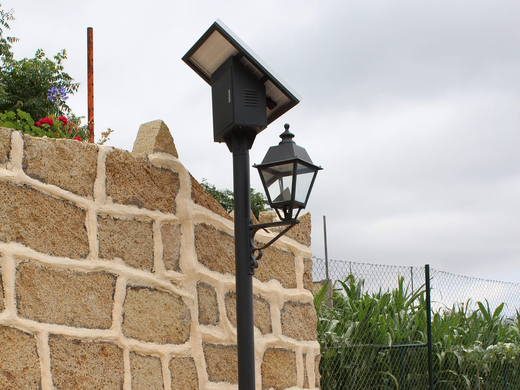 farola fotovoltaica cercana a muro de piedra caliza color beige. Al fondo cielo nuboso