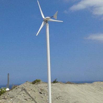 imagen de pequeño aerogenerador blanco. Terreno arenoso y cielo azul dominante en la escena