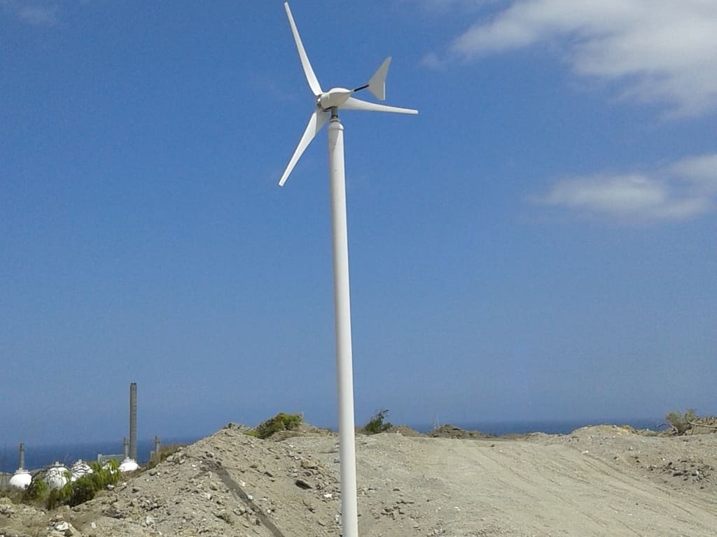 imagen de pequeño aerogenerador blanco. Terreno arenoso y cielo azul dominante en la escena