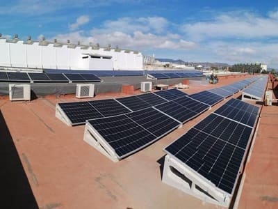 paneles solares sobre techo de instalación industrial. Techo de color teja. Al fondo cielo y nubes.