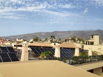 Placas solares sobre complejo de apartamentos. Techo en primer término y chimeneas