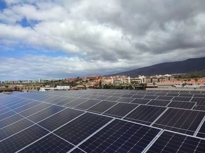 placas solares sobre techo de establecimiento hotelero. Al fondo urbanización turística, montaña y cielo nuboso
