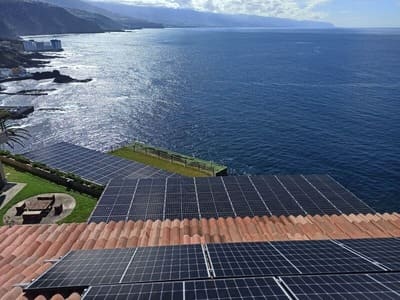 placas solares sobre tejado color teja. Al fondo el mar en día soleado